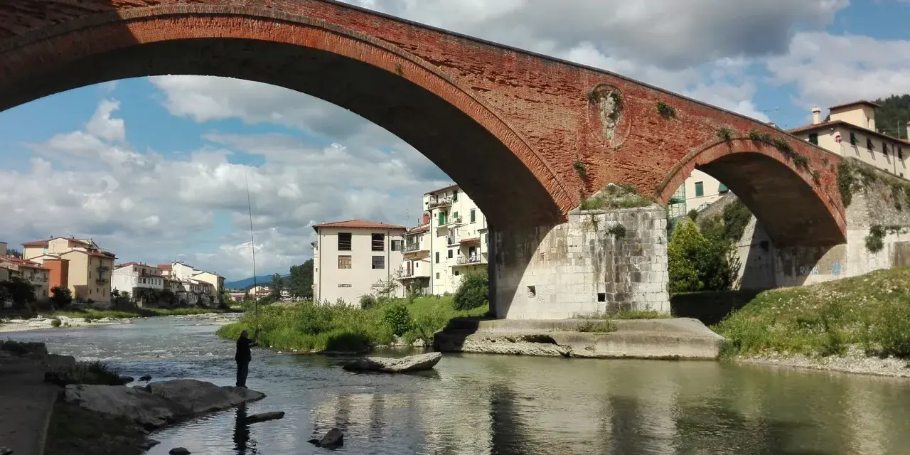 Ponte Mediceo a Pontassieve, cosa vedere: un pescatore sul fiume Sieve sotto l'arco in mattoni rossi, con case colorate sullo sfondo.