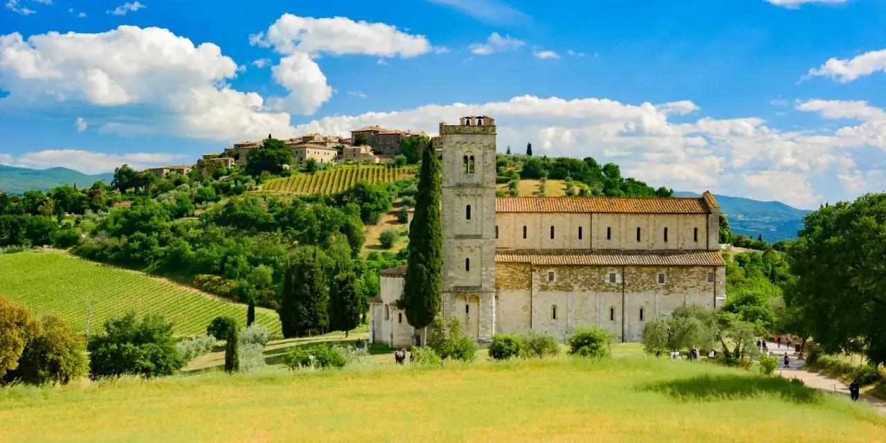 Abbazia di Sant'Antimo, un gioiello romanico immerso nel verde della Toscana, con vigneti e un borgo sullo sfondo.