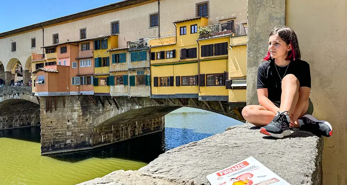 Ragazza con capelli rosa seduta sul Ponte Vecchio a Firenze, con una guida per bambini in primo piano.