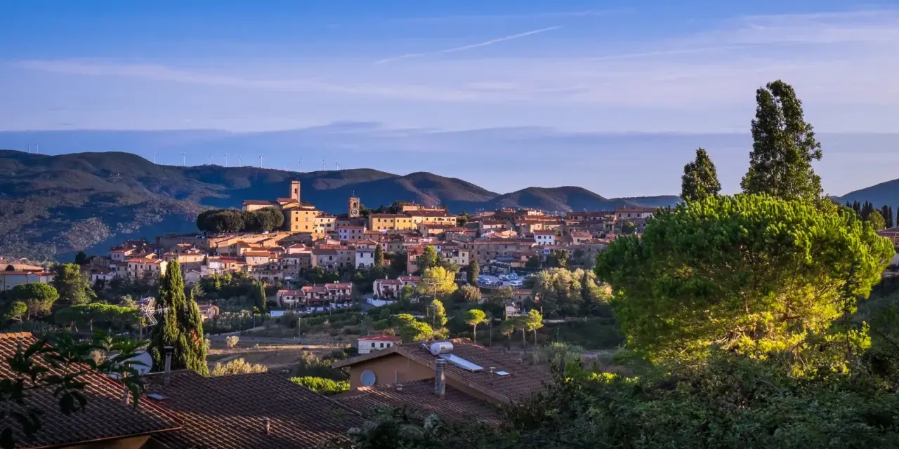 Panoramica di Montescudaio cosa vedere: borgo toscano con case in pietra, chiese e torri, immerso nel verde collinare sotto un cielo azzurro.