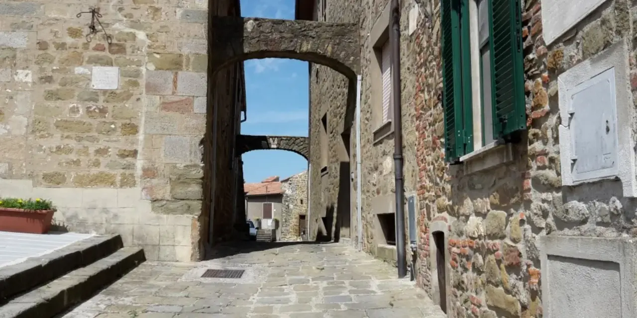 Un vicolo suggestivo a Vetulonia, tra antiche mura di pietra e archi che incorniciano il cielo azzurro. Scopri cosa vedere in questo borgo storico.