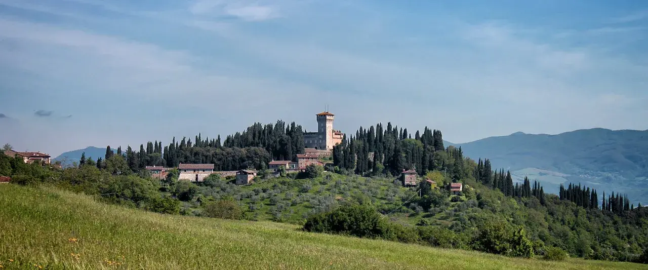 Un borgo collinare con un castello domina il paesaggio toscano di Scarperia e San Piero, circondato da cipressi e ulivi.