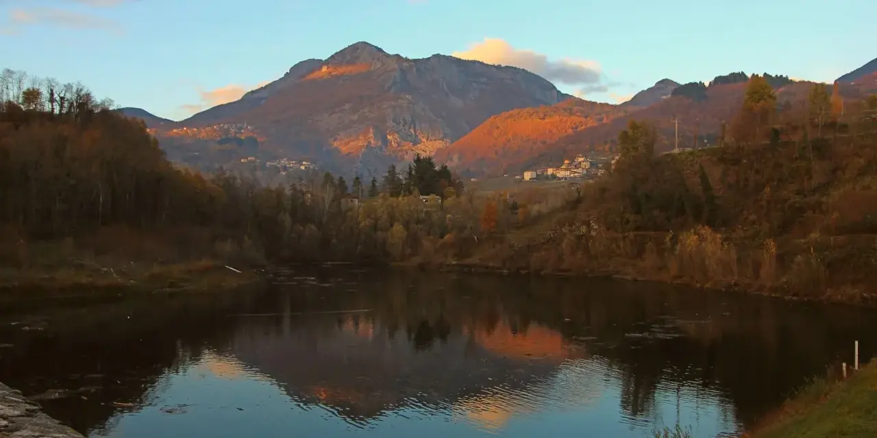 Tramonto dorato sulle montagne vicino a Villa Collemandina, con un lago che riflette il paesaggio autunnale.