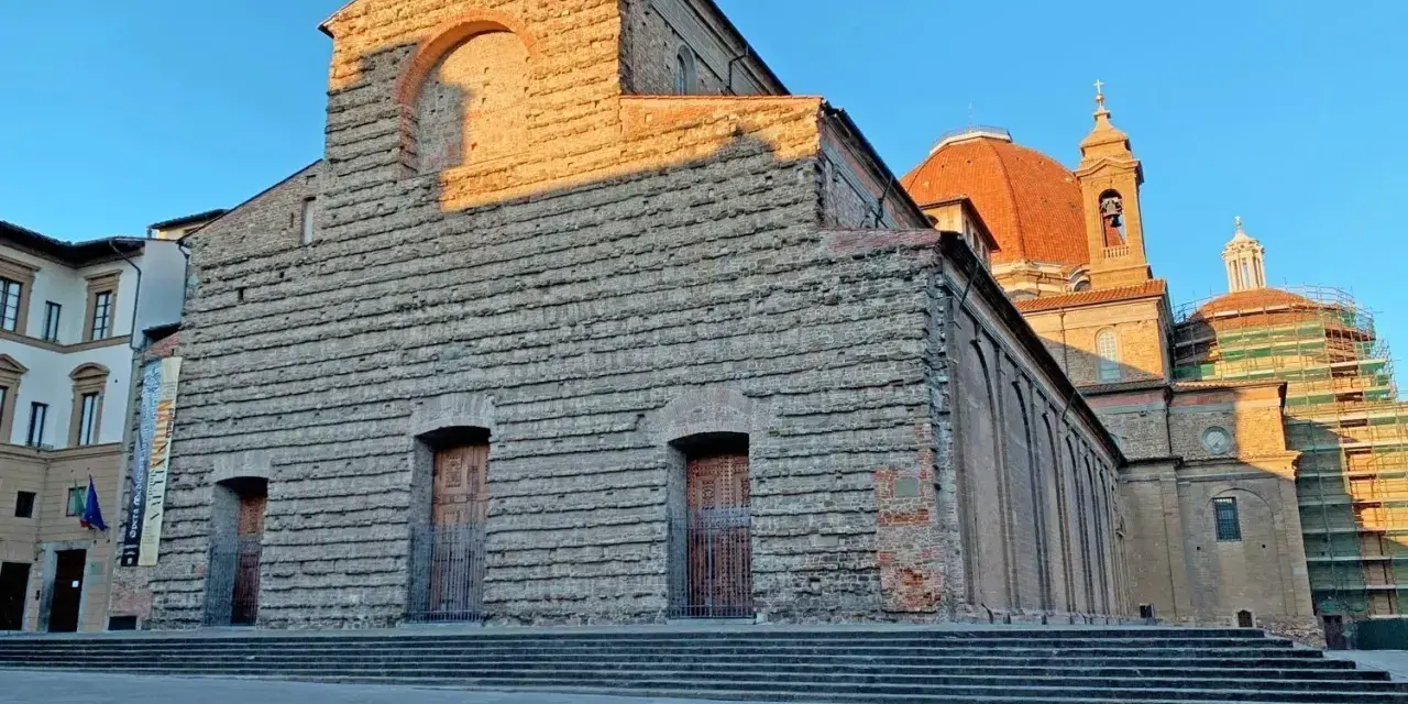 La facciata in pietra di San Lorenzo a Firenze, con la cupola arancione che domina il cielo azzurro.