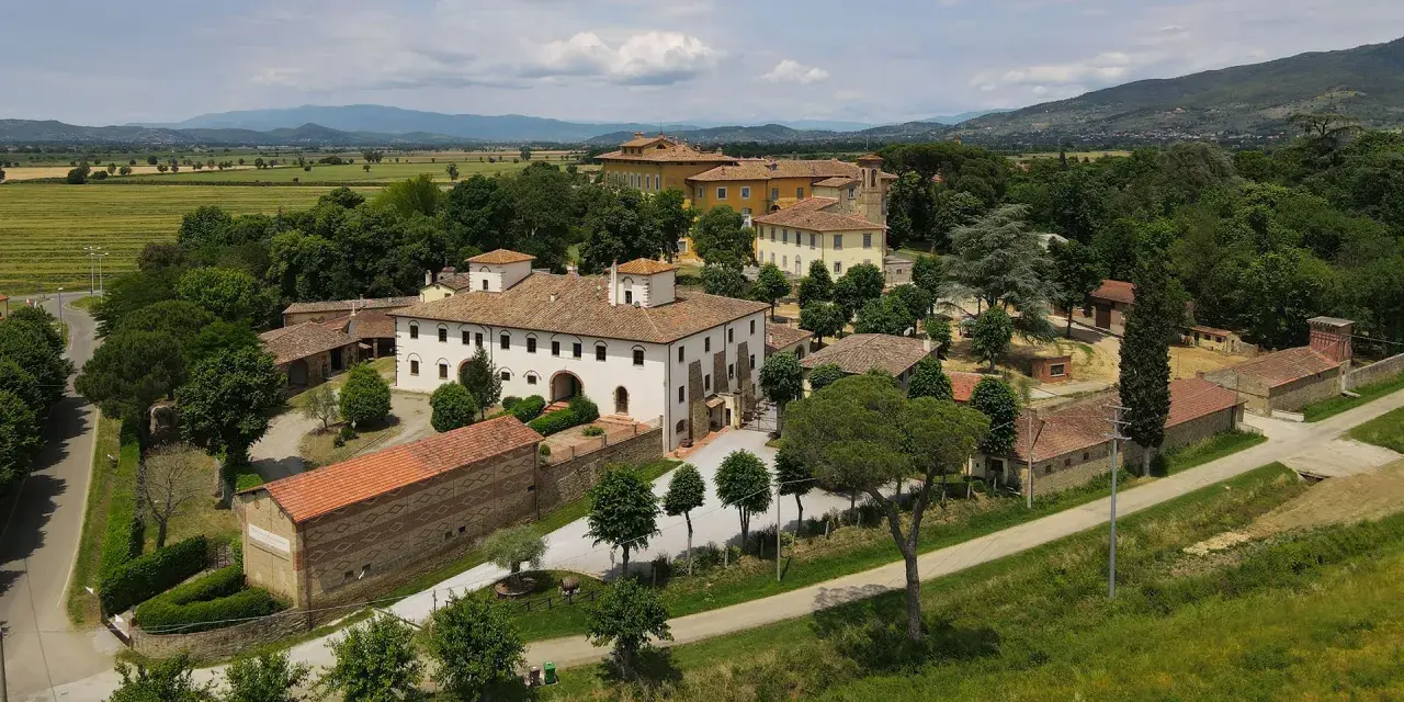 La Tenuta Frassineto, un complesso di edifici storici immerso nel verde, con campi coltivati e colline sullo sfondo.