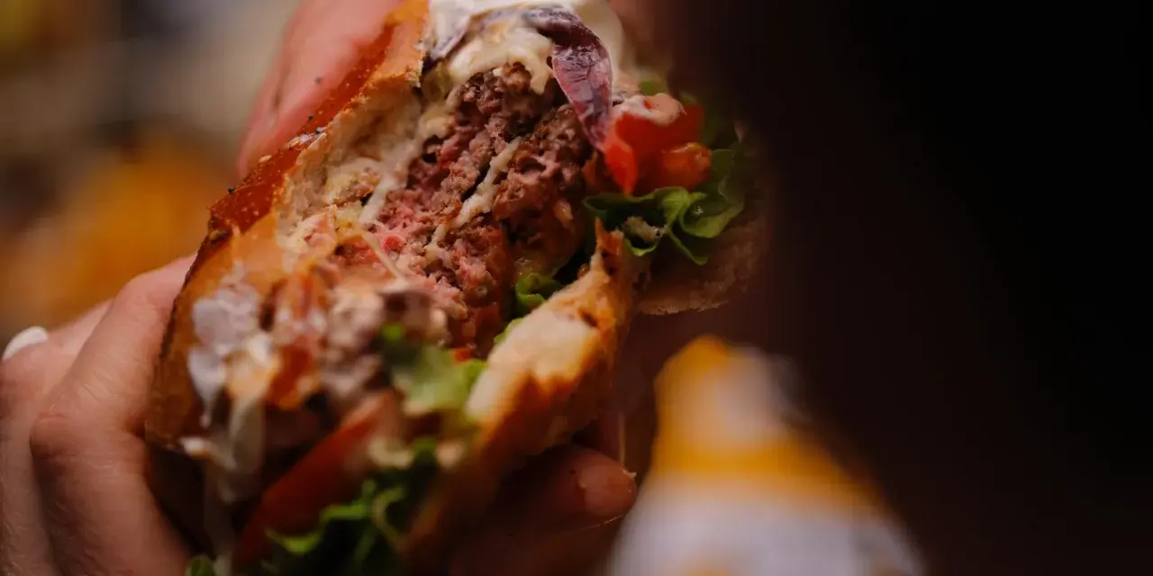 Mani che stringono un succulento hamburger, un'esplosione di sapori tipica dello street food ad Arezzo.