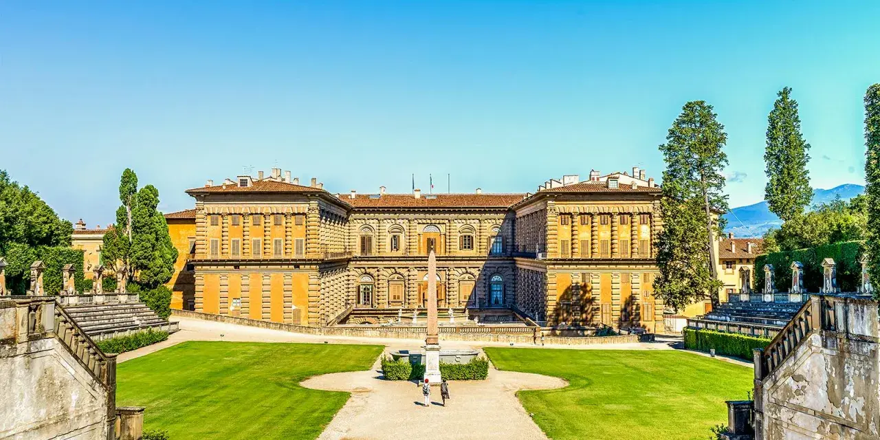 Il maestoso Palazzo Pitti si staglia contro un cielo azzurro, circondato da giardini curati e scalinate imponenti.