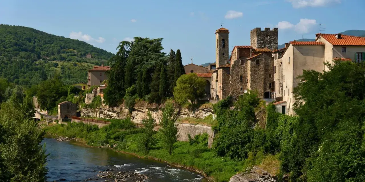 Borgo medievale di Subbiano, Arezzo, con il fiume che scorre ai suoi piedi e il verde rigoglioso che abbraccia le antiche pietre.