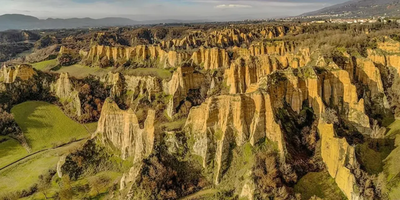 Paesaggio surreale nella provincia di Arezzo, con calanchi dorati che si ergono tra colline verdi e alberi spogli.
