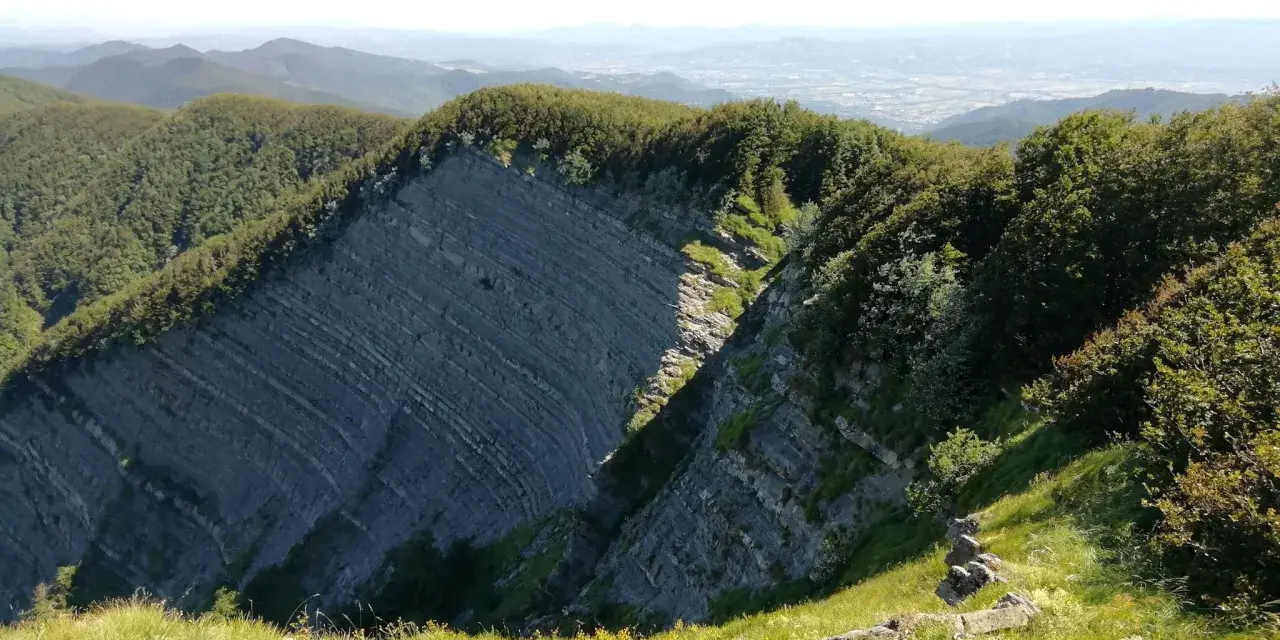 Panoramica mozzafiato sull'Alpe della Luna, con rocce stratificate che si ergono tra boschi rigogliosi e un cielo azzurro.