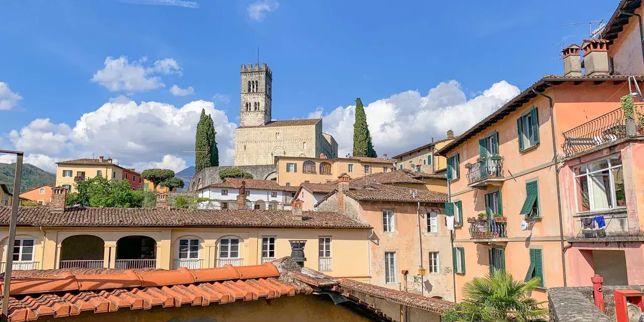 Panoramica di Barga, Lucca, con case colorate e il Duomo in cima alla collina sotto un cielo azzurro con nuvole bianche.