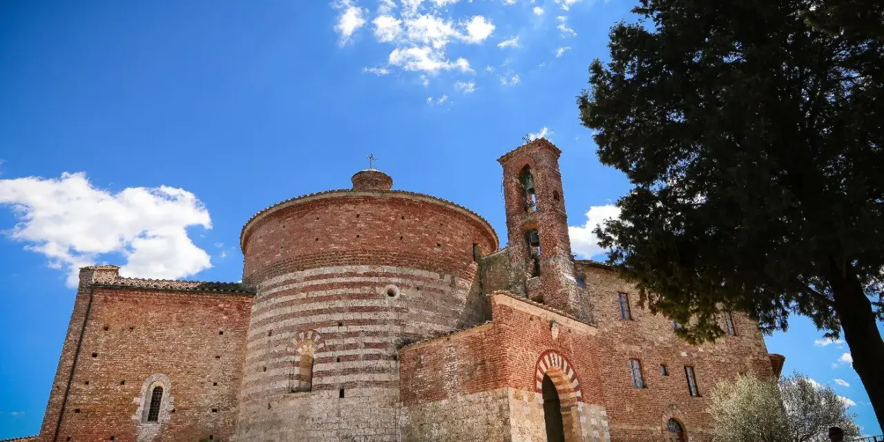 L'abbazia di San Galgano, con la sua rotonda in mattoni a fasce bianche e rosse, si staglia sotto un cielo azzurro con nuvole bianche.