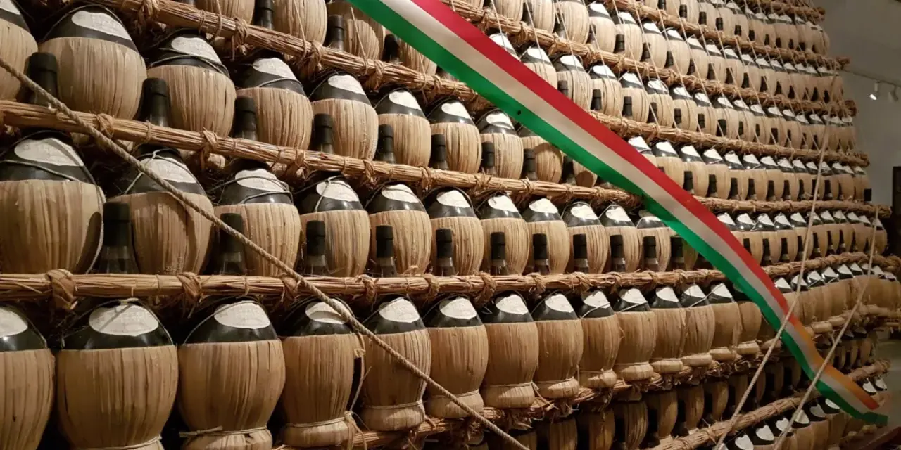 Una grande esposizione di bottiglie di vino impagliate, forse un omaggio alla tradizione della villa poggio reale rufina, con un tricolore italiano che le attraversa.