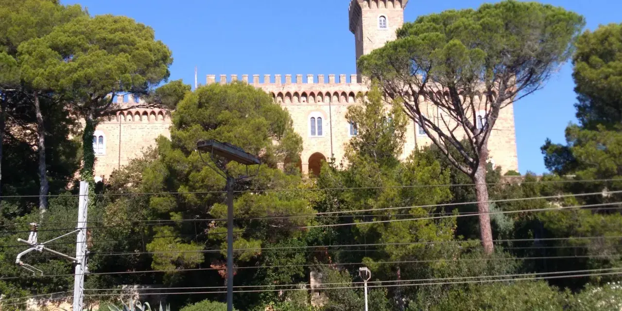 Il Castello Pasquini, con la sua torre imponente, emerge tra alberi verdi e un cielo azzurro.