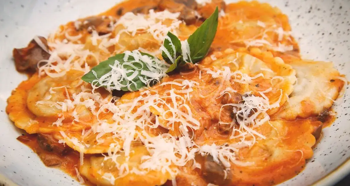 Tordelli versiliesi in un piatto bianco, conditi con sugo rosso, funghi, parmigiano grattugiato e basilico fresco.