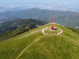 La croce del Pratomagno domina un paesaggio verdeggiante, con montagne boscose e una città in lontananza.