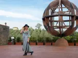 Donna con cappello nero ammira l'Uomo Vitruviano in una sfera di legno, un'opera iconica da vedere a Vinci, con colline verdi sullo sfondo.
