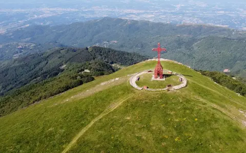 La croce del Pratomagno domina un paesaggio verdeggiante, con montagne boscose e una città in lontananza.