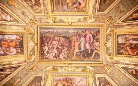 Soffitto affrescato con scene storiche e figure mitologiche, un capolavoro che evoca la grandezza del **Palazzo Vecchio**.