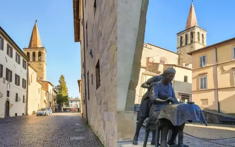 Statua di donne al lavoro, con campanili e palazzi storici sullo sfondo. Un assaggio di cosa vedere a Sansepolcro.