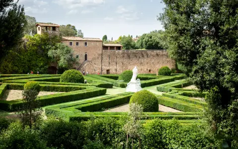 Giardini geometrici a San Quirico d'Orcia con statua bianca e edifici storici sullo sfondo.