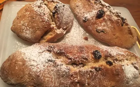 Tre panini aretini dorati, cosparsi di zucchero a velo e uvetta, pronti per essere gustati.