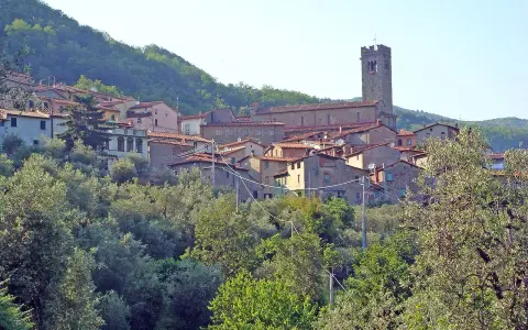 Antica villa basilica con torre campanaria, immersa nel verde di una collina toscana.