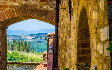 Arco in pietra che incornicia un panorama collinare toscano, con cipressi e vigneti, tipico dei borghi del Chianti.
