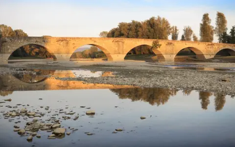 Ponte romanico con archi a tutto sesto, riflesso sull'acqua calma. I Setteponti di Arezzo, un'antica via, abbraccia la campagna toscana.