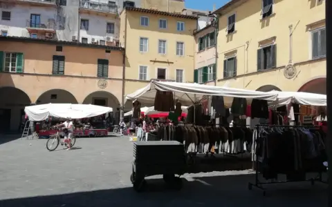 Mercato all'aperto nella piazza delle vettovaglie, con bancarelle di abbigliamento e persone che passeggiano.
