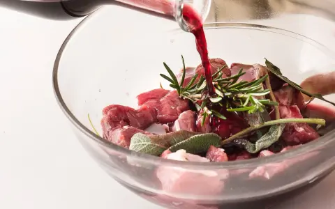 Vino rosso versato su cubetti di carne e aromi per macerare cinghiale.