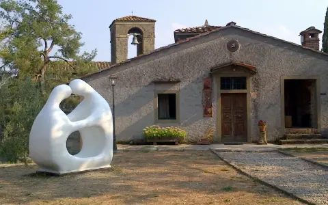 Scultura moderna di due figure abbracciate, simbolo di romena accoglienza, davanti a un edificio con campanile.