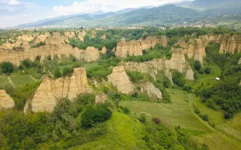 Le suggestive balze del Valdarno, scolpite dal tempo, si ergono tra verdi colline e un borgo in lontananza.
