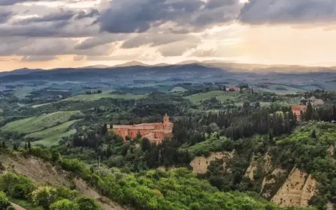 Un imponente complesso monastico, il Monte Oliveto Maggiore, si erge tra dolci colline toscane sotto un cielo drammatico.