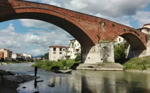 Ponte Mediceo a Pontassieve, cosa vedere: un pescatore sul fiume Sieve sotto l'arco in mattoni rossi, con case colorate sullo sfondo.