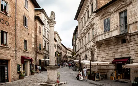 A stone column with a lion statue stands in a cobblestone street lined with historic buildings and shops.