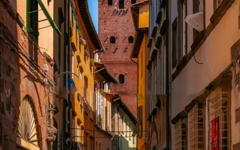 Un vicolo stretto a Lucca con edifici colorati e la torre Guinigi che svetta in lontananza.