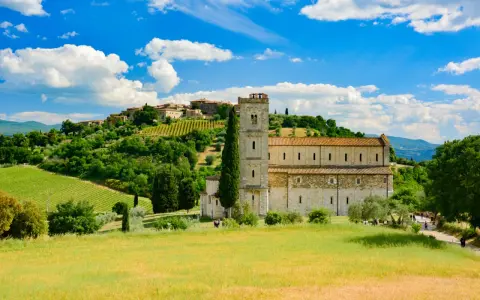 Abbazia di Sant'Antimo, un gioiello romanico immerso nel verde della Toscana, con vigneti e un borgo sullo sfondo.