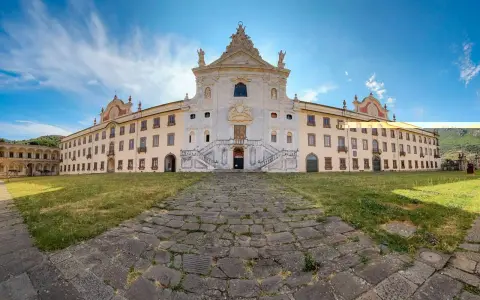 La maestosa Certosa di Calci si erge sotto un cielo azzurro, con un sentiero di pietra che conduce alla sua imponente facciata.