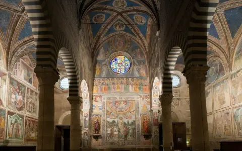 Interno del duomo di San Gimignano, con affreschi medievali che narrano storie sacre, volte a crociera a strisce bianche e nere e un rosone colorato.