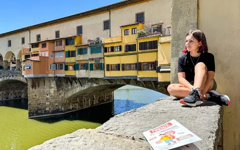 Ragazza con capelli rosa seduta sul Ponte Vecchio a Firenze, con una guida per bambini in primo piano.