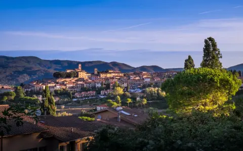 Panoramica di Montescudaio cosa vedere: borgo toscano con case in pietra, chiese e torri, immerso nel verde collinare sotto un cielo azzurro.