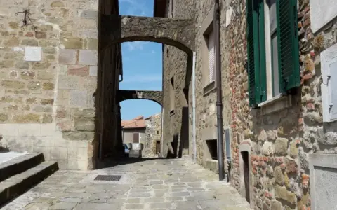 Un vicolo suggestivo a Vetulonia, tra antiche mura di pietra e archi che incorniciano il cielo azzurro. Scopri cosa vedere in questo borgo storico.