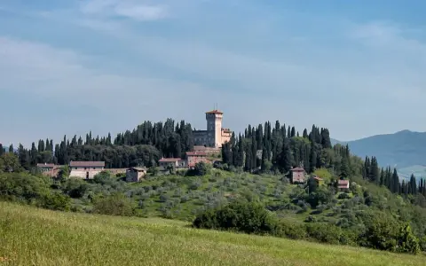 Un borgo collinare con un castello domina il paesaggio toscano di Scarperia e San Piero, circondato da cipressi e ulivi.