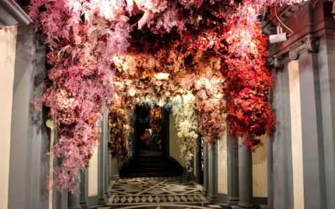 Ingresso fiorito, un arco di fiori rossi e rosa che ricorda l'antica farmacia di Firenze.