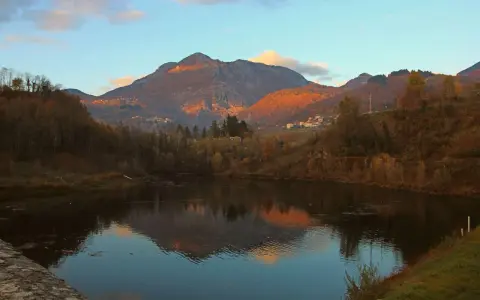 Tramonto dorato sulle montagne vicino a Villa Collemandina, con un lago che riflette il paesaggio autunnale.