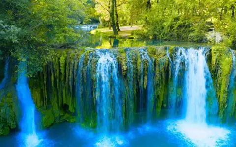 Cascata rigogliosa nel Val d'Arno, con acqua azzurra che scende su rocce ricoperte di muschio verde.