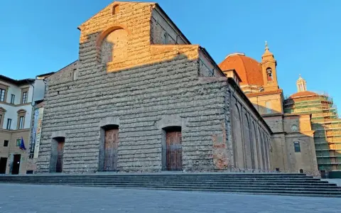La facciata in pietra di San Lorenzo a Firenze, con la cupola arancione che domina il cielo azzurro.