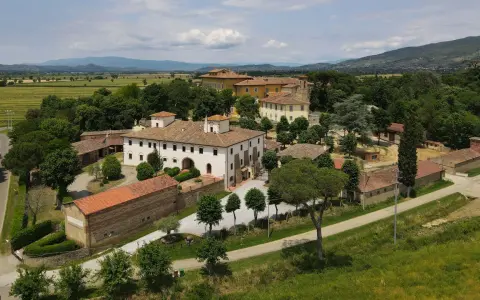 La Tenuta Frassineto, un complesso di edifici storici immerso nel verde, con campi coltivati e colline sullo sfondo.