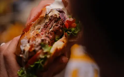 Mani che stringono un succulento hamburger, un'esplosione di sapori tipica dello street food ad Arezzo.